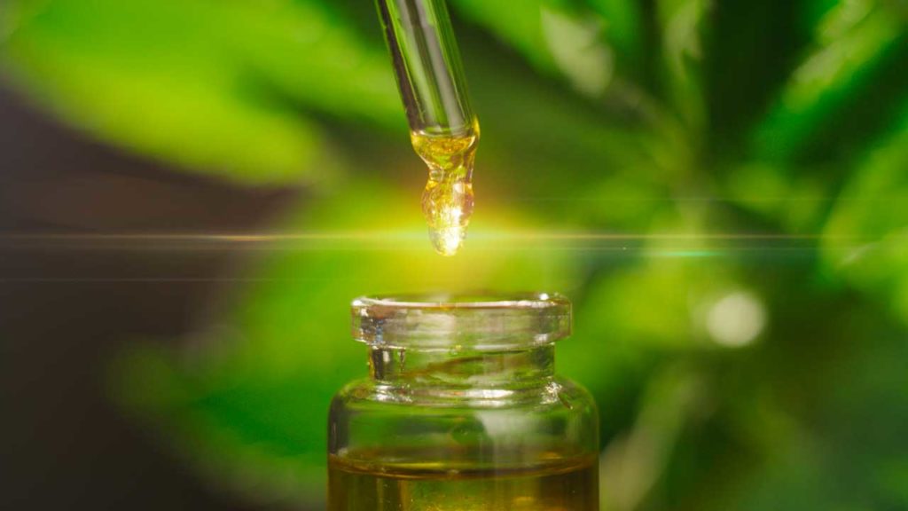 A close-up photo of the best CBD oil for pain in a dropper over a glass bottle with the oil