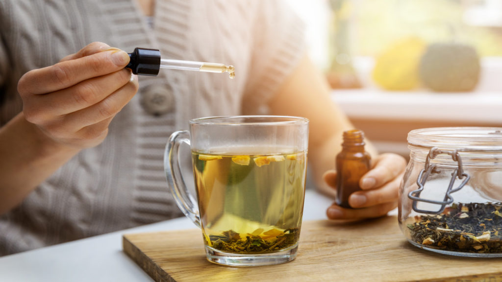  A woman using CBD for stress and adding organic CBD oil to her tea to alleviate symptoms of stress.