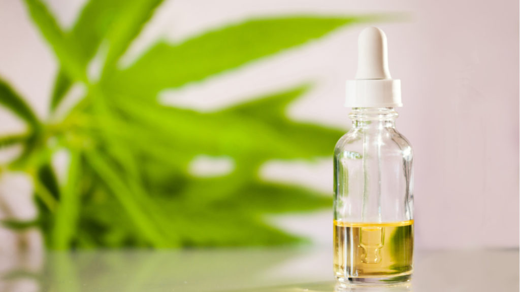  A glass bottle containing CBD dosage tincture placed against a white background with a leaf behind
