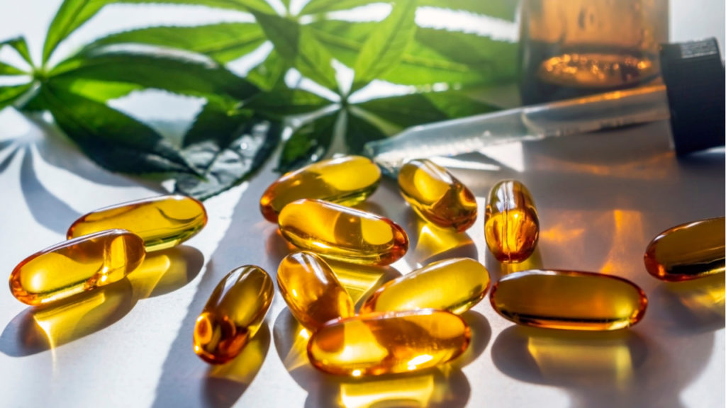 Gold colored CBD dosage capsules lying on a table with sunlight shining on them from the background
