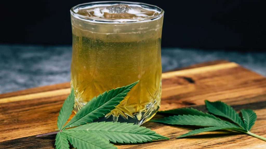Two cannabis plant leaves next to an ice cold cannabis-infused drink made by mixing CBD and alcohol