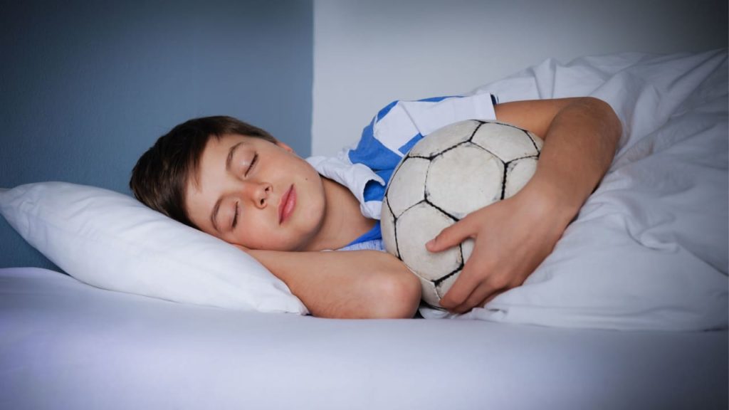 A young boy is asleep in bed, holding a soccer ball close to him.